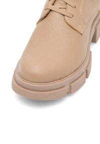 Beżowy skórzany but z okrągłym noskiem, teksturowaną cholewką i grubą gumową podeszwą. Posiada sznurowane zapięcie i minimalistyczne detale.