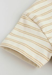 Tissu couleur crème avec de fines rayures horizontales beiges, montrant un détail de manche pliée et des coutures.