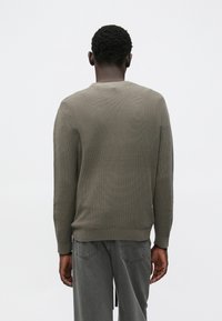 Khaki tekstureret sweater med rund halsudskæring, ribstrikkede manchetter og kant. Brugt over grå vidde bukser, set bagfra.