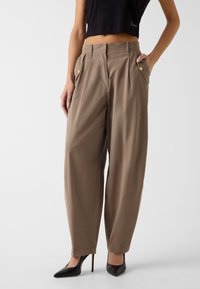 Bruine wijde pantalon met plooien en zijzakken met gouden hardware accenten, gemaakt van lichtgewicht stof.