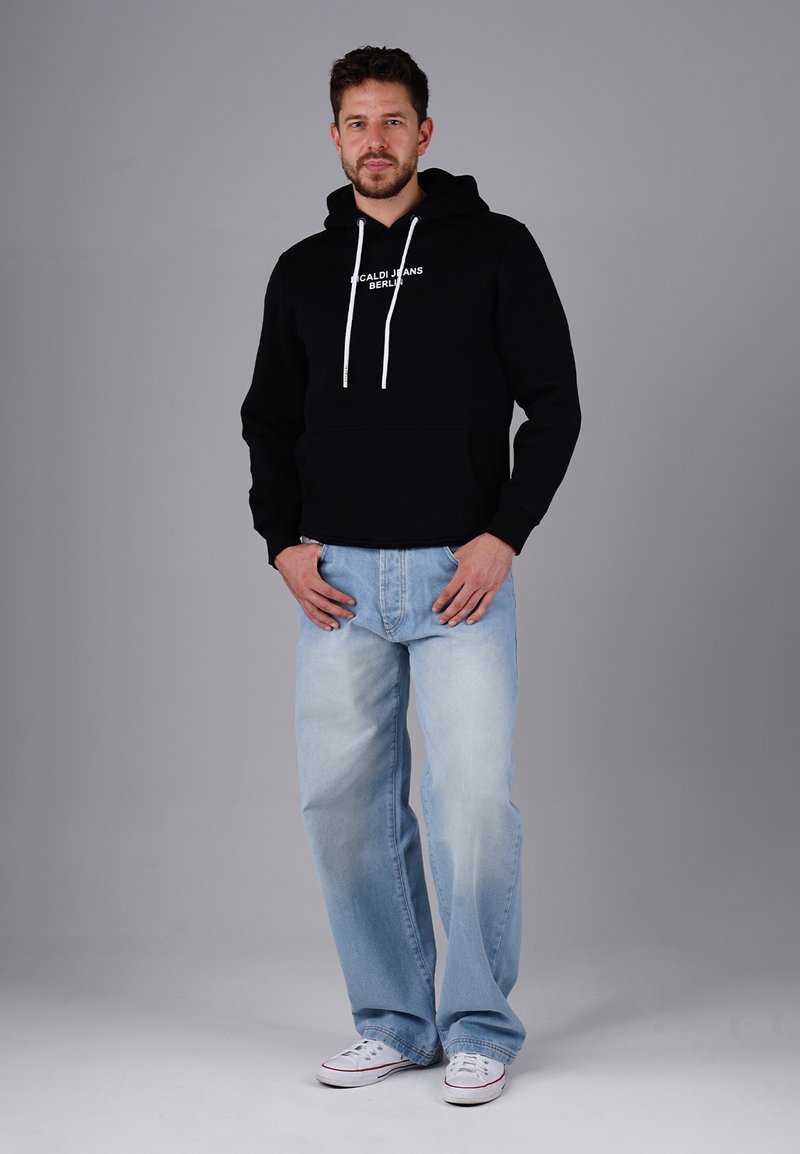 Schwarzer Baumwoll-Hoodie mit weißem Text, kombiniert mit hellblauen, locker sitzenden Jeans. Weiße Sneakers mit roten Akzenten. Einfaches, entspanntes Design.