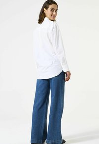 Witte overhemd met kraag, gecombineerd met een wijde spijkerbroek in blauw met zijversieringen. Soepele stof en een ontspannen pasvorm.