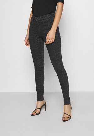 Pantalones ajustados de mezclilla con estampado de leopardo negro, con un corte slim, diseño de cinco bolsillos y una textura sutil. Combinados con sandalias negras de tacón alto y tiras.