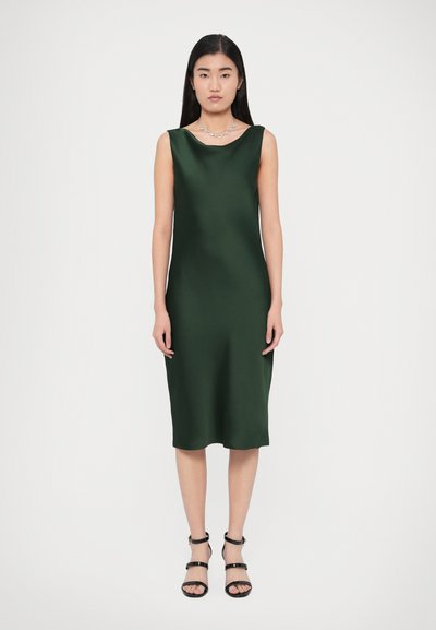Green satin sleeveless dress with a scoop neckline, midi length, and a smooth texture, paired with black strappy sandals and a necklace.