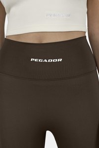 Barna, magas derékú leggingsek rugalmas anyagból, a deréknál egy fehér "PEGADOR" logóval és sima, testhezálló sziluettel.