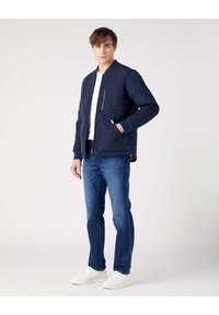 Granatowa pikowana kurtka bomberka z zapięciem na zamek błyskawiczny i bocznymi kieszeniami, zestawiona z niebieskimi dżinsami i białymi trampkami na neutralnym tle.