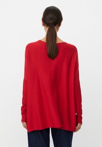 Červený oversize svetr vyrobený z jemného pleteného materiálu, s širokým výstřihem, dlouhými rukávy a volným střihem. Jednoduchý design, bez vzorů.