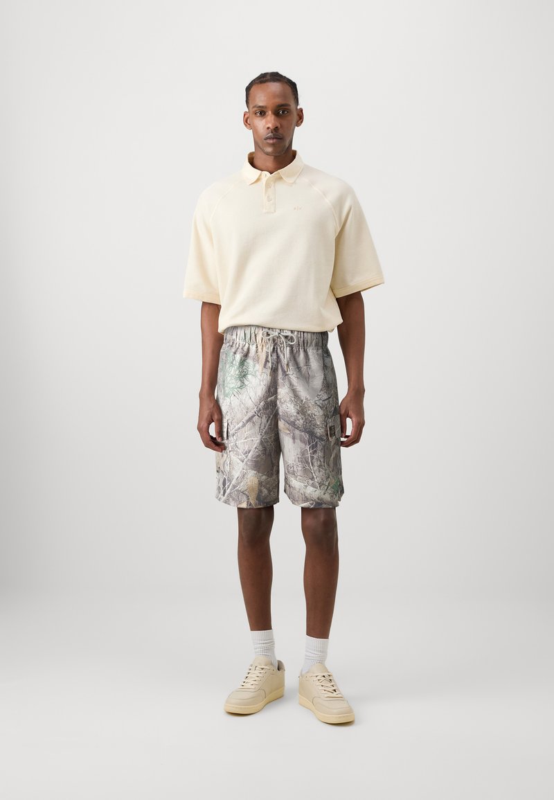 Light yellow polo shirt with a textured pattern, paired with camouflage cargo shorts featuring greens, browns, and a drawstring waistband.