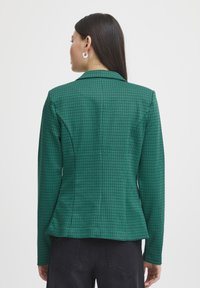 Zelený kostičkovaný blazer se strukturovaným designem, dlouhými rukávy a přiléhavým střihem, se zářezovým límcem a jemnou texturou.