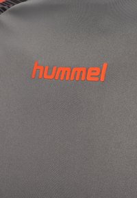 Grijze stof met een textuur en een feloranje "hummel" merklogo in kleine letters gedrukt.
