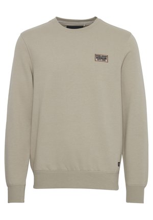 Světle béžová mikina s kulatým výstřihem, s žebrovanými manžetami a spodním lemem, s malou značkovou nášivkou na horní levé části předního dílu. Měkký materiál z bavlněné směsi.