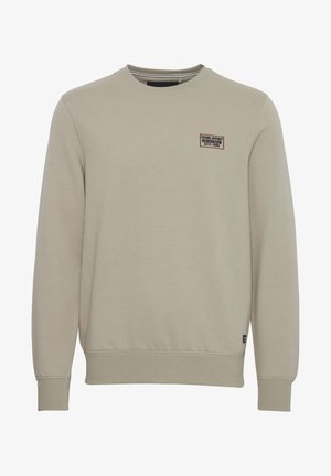 Hellbeige Sweatshirt mit Rundhalsausschnitt, gerippten Bündchen und Saum, das einen kleinen Markierungs-Patch auf der oberen linken Vorderseite trägt. Weicher Materialmix aus Baumwolle.
