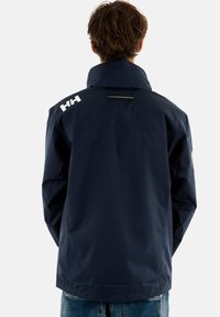 Chubasquero impermeable navy con alto cuello, textura suave y logotipo en contraste en blanco. Presenta un canesú trasero y una línea de acento sutil.