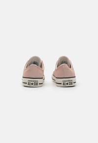 Pink suede Converse sneakers with a white rubber sole, black stripes, and "All Star" branding on the heel. Rounded toe design.