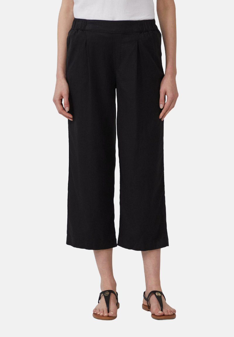 Zwarte wijde broek met een geplooide voorkant, elastische tailleband en lichtgewicht stof. Gecombineerd met bruine slippers.