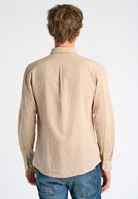 Camisa de manga larga de color marrón hecha de tejido texturizado, con un cuello puntiagudo, puños abotonados y un detalle de canesú en la parte posterior.