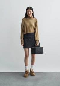 Suéter de cuello alto color beige oversize, mini falda de mezclilla oscura, calcetas blancas, botas marrones con borde de piel y bolso negro con patrón geométrico.