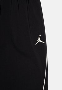 Melni šorti, izgatavoti no viegla auduma, ar izšūtu baltu Jumpman logo un baltu sānu svītru kontrastam.