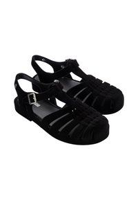 Sandales noires en suede doux avec des découpes, maintenues par une bride ajustable à la cheville et une semelle plate.