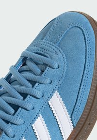 Modre semižne superge z belimi zigzag črtami, ravnimi vezalkami in gumijastim podplatom. Imajo šivane detajle na zgornjem delu.