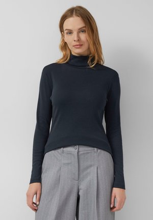 Diepblauwe coltrui gemaakt van gladde, elastische stof; lange mouwen; aansluitend ontwerp; gecombineerd met lichtgrijze trousers met streepjes.