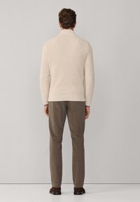 Beige gebreide trui met een hoge kraag, gecombineerd met olijfgroene broek. De outfit heeft een gestructureerde stof en een rechte pasvorm.