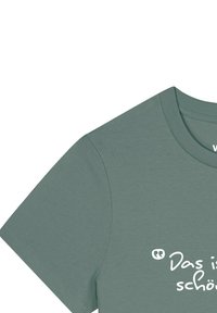 Groene katoenen t-shirt met korte mouwen, ronde halslijn, met witte tekst "Das ist schön" op de voorkant. Soepele textuur.