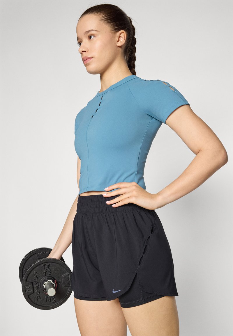 Conjunto atlético que incluye una camiseta ajustada de manga corta azul claro y pantalones cortos negros con una abertura lateral, sosteniendo un dumbbell negro en una mano.
