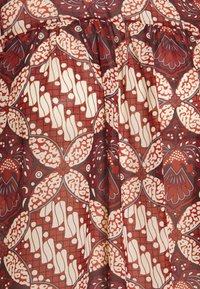 Tessuto rosso e crema con pattern floreali e geometrici, caratterizzato da dettagli intricati e una texture leggera e liscia.