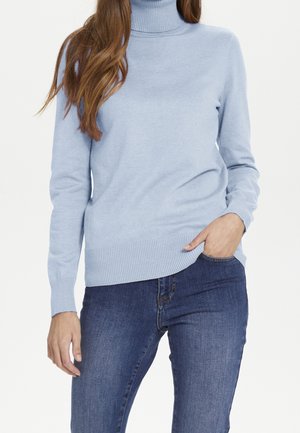 Light blue turtleneck sweater in soft knit fabric, featuring ribbed cuffs and hem, paired with dark blue jeans. Model has one hand in pocket.