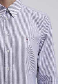 Randig skjorta i ljus lila och vit, med knapp-down krage, två framknappar och en liten broderad logga på bröstet.