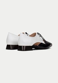 Chaussures bicolores avec un bout en cuir noir et un talon blanc, dotées d'un petit talon carré et de lacets. Texture lisse avec des détails de couture clairs.
