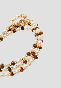 Three-strand bracelet with white pearls, brown wooden beads, and small gold beads, featuring a gold clasp and adjustable chain.