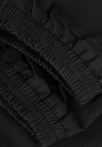 Primer plano de puños de tela elástica negra con costuras detalladas y textura fruncida.