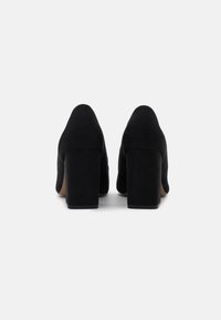 Schwarze Wildleder-Blockabsatzschuhe mit einem spitzen Zehen Design. Die Absätze sind breit und stabil und bieten eine strukturierte Oberfläche.