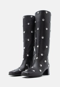 Μαύρες δερμάτινες μπότες μέχρι το γόνατο με ασημένιες λεπτομέρειες, τετράγωνη μύτη, χοντρό τακούνι, λεία υφή και φερμουάρ στο πλάι.