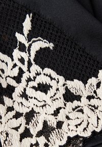 Zwarte stof met een witte bloemenkant overlay. Het kant heeft ingewikkeld geborduurde rozen en een gestructureerd, open weefpatroon.