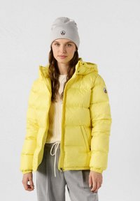 Giacca a vento gialla con cappuccio, caratterizzata da un design trapuntato e polsini elasticizzati. Accompagnata da un berretto lavorato a maglia grigio chiaro.
