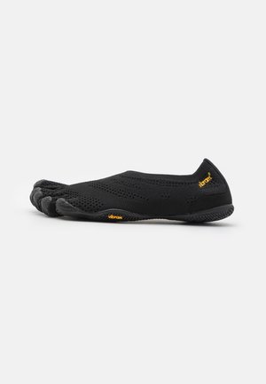 Chaussure minimaliste noire pieds nus avec compartiments individuels pour chaque orteil, tige en tricot respirant et semelle en caoutchouc Vibram, vue de côté sur fond blanc.