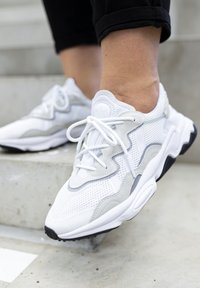 Zapatillas deportivas de malla blanca y ante con acentos grises, que presentan un diseño curvado, cordones planos y una suela de goma negra.