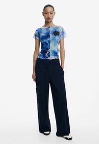 Top astratto blu a maniche corte, abbinato a pantaloni larghi blu navy. Il top presenta un tessuto morbido e leggero.