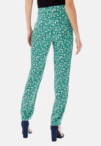 Green patterned trousers with a slim fit, featuring abstract shapes in pink, white, and navy. Smooth fabric with an elastic waistband.