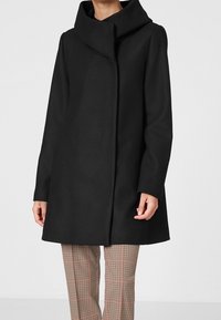 Cappotto nero con colletto alto e design a frontale aperto, realizzato in un materiale testurizzato. Il cappotto ha maniche lunghe e una silhouette dritta.