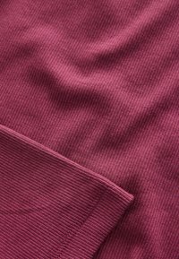 Close-up of ribbed fabric texture in dark pink, showing stitching and folds on a textile surface.