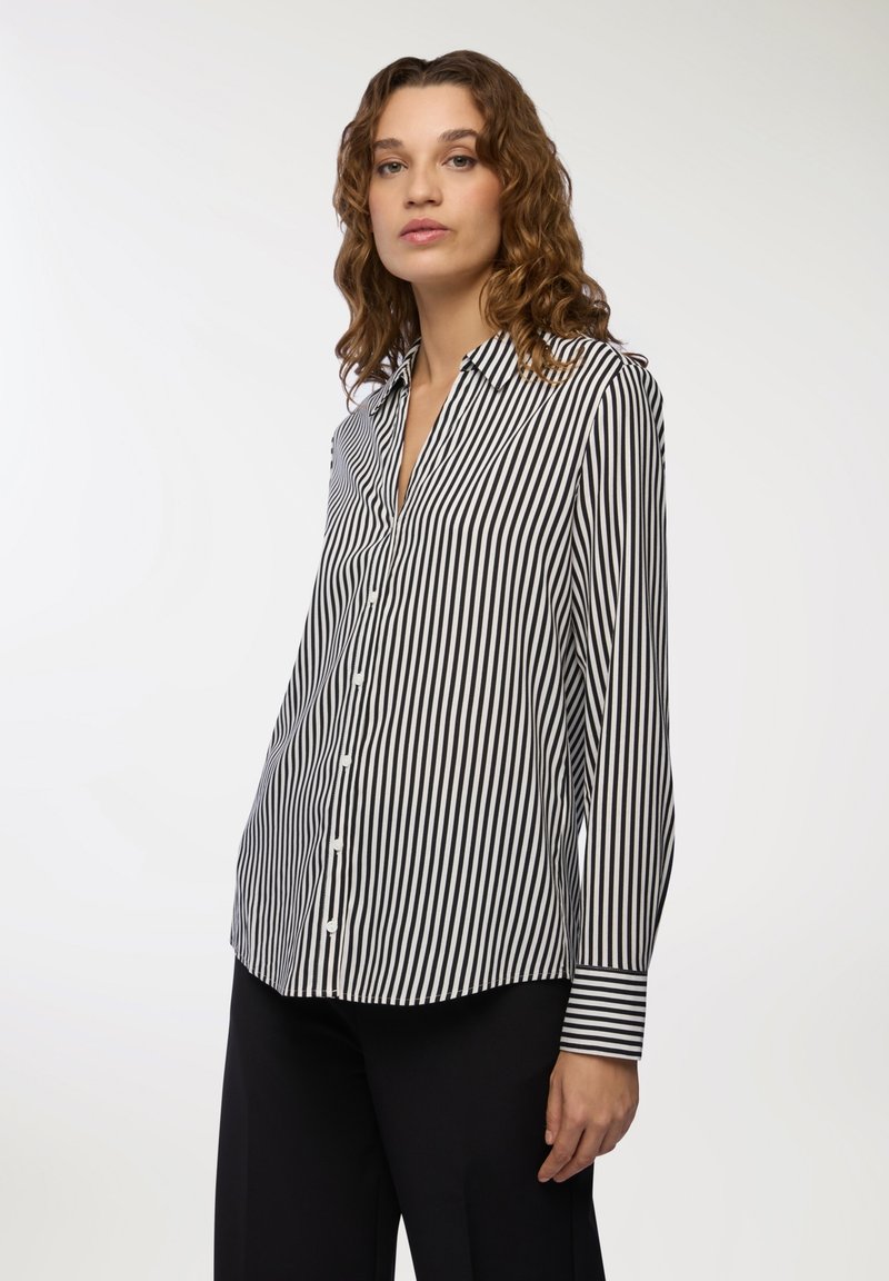 Camicia button-up in righe verticali bianche e nere, realizzata in tessuto morbido, con colletto a punta e maniche lunghe con dettagli ai polsini.