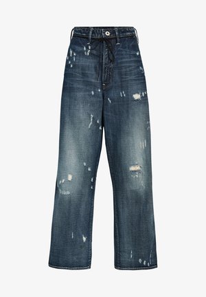 Tummansiniset farkut, joissa on löysä istuvuus, näyttävät kulutuskohdat, hapsutetut reunat ja nyöri vyötäröllä.