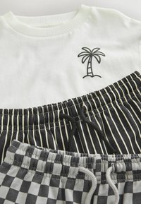 T-shirt blanc col rond avec un motif de palmier noir, associé à un short taille élastique rayé et à carreaux noir et blanc.