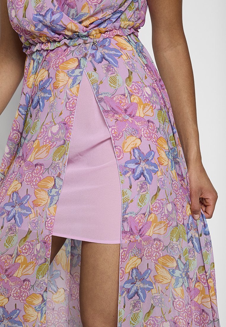 Zbliżenie na sukienkę w kwiatowy wzór z fioletowymi, różowymi, pomarańczowymi i niebieskimi kwiatami na różowej podszewce, z rozcięciem z przodu i z detalem zapięcia.
