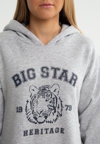 Pilkas gobtuvas su dideliu juodu tigru ir "BIG STAR HERITAGE" tekstu tamsiai mėlyna spalva, su pūkuotomis rankovėmis ir laisvu siluetu.