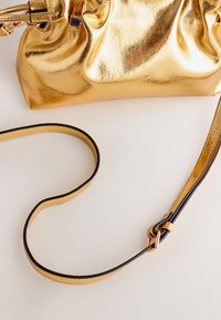 Geantă clutch aurie metalizată cu textură cutată, prevăzută cu o curea accentuată în negru. Include un design elegant pliabil și accesorii decorative.